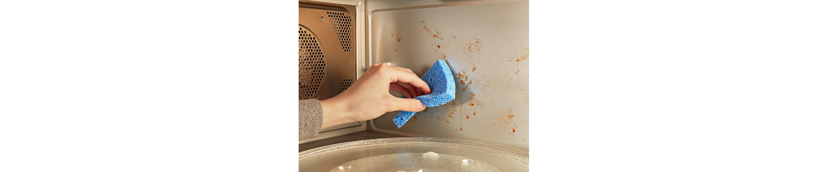 Person wiping splattered food off a microwave with a sponge