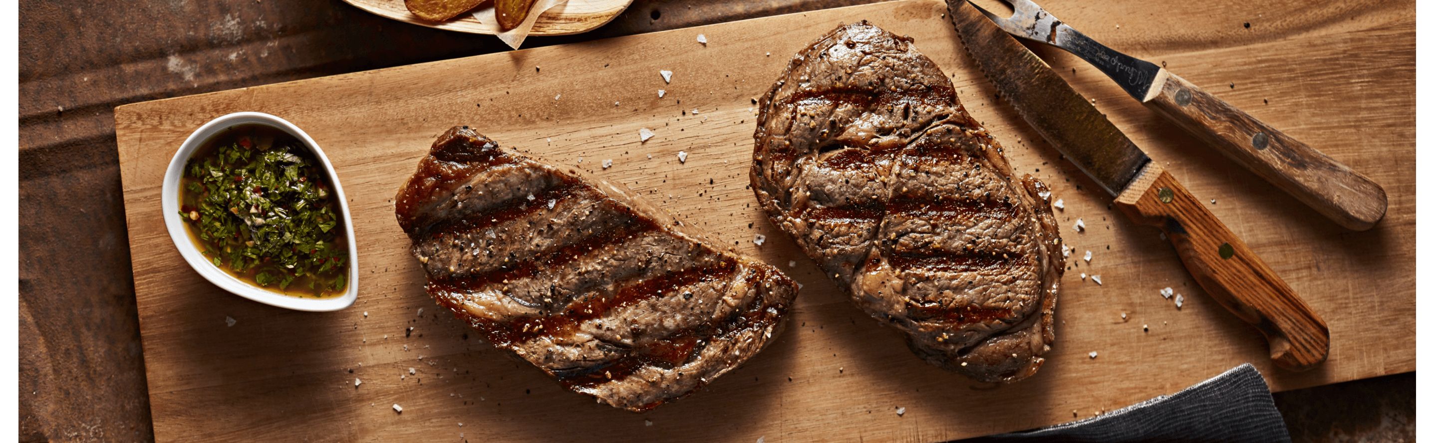 Two grilled steaks on a cutting board