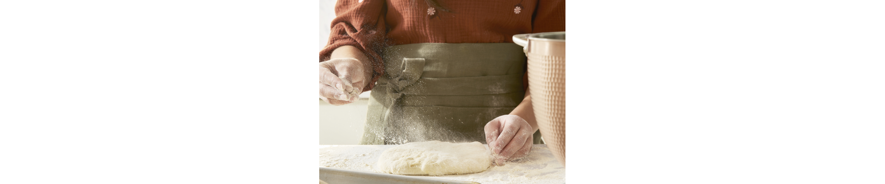 A person lightly flouring risen dough on a work surface