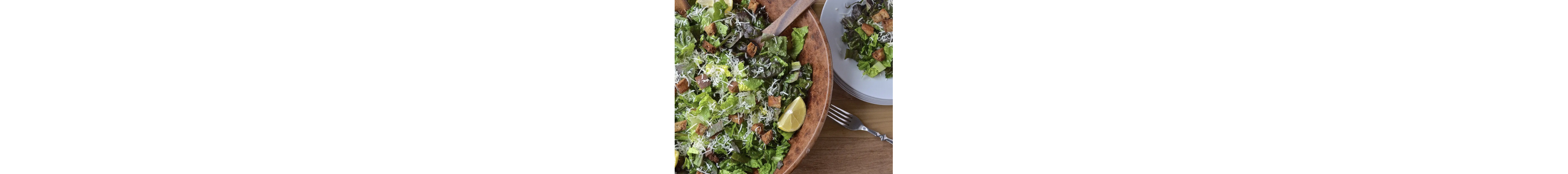 A serving bowl filled with a crisp salad topped with limes and shredded cheese.