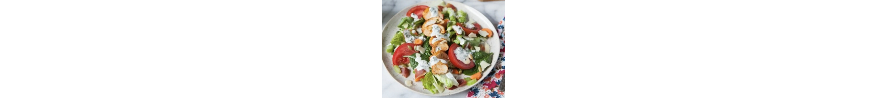 Leafy greens and tomato wedges drizzled with ranch dressing.