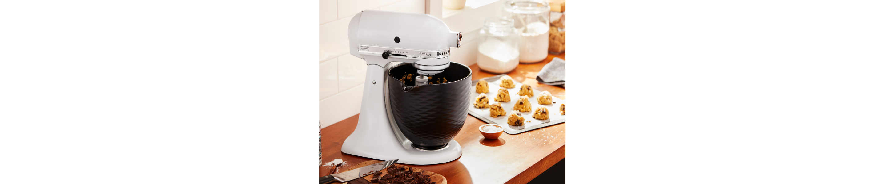 A white KitchenAid® stand mixer next to a sheet of cookie dough 