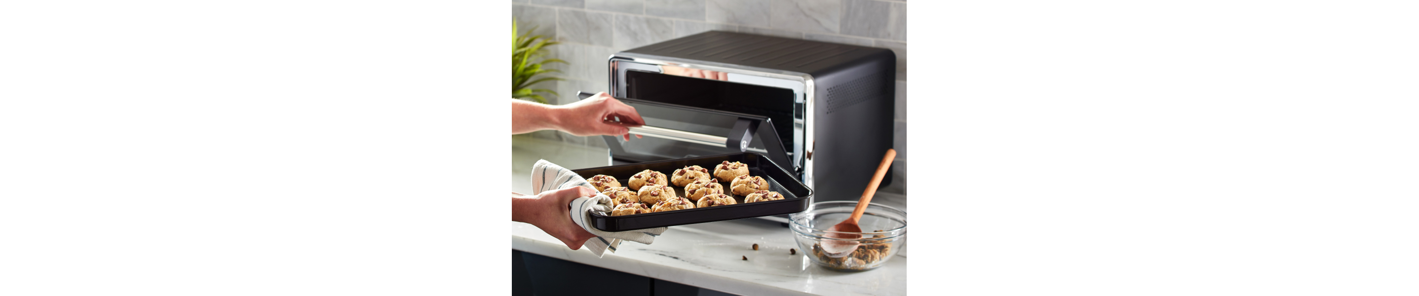 A person placing a sheet with cookie dough into a countertop oven