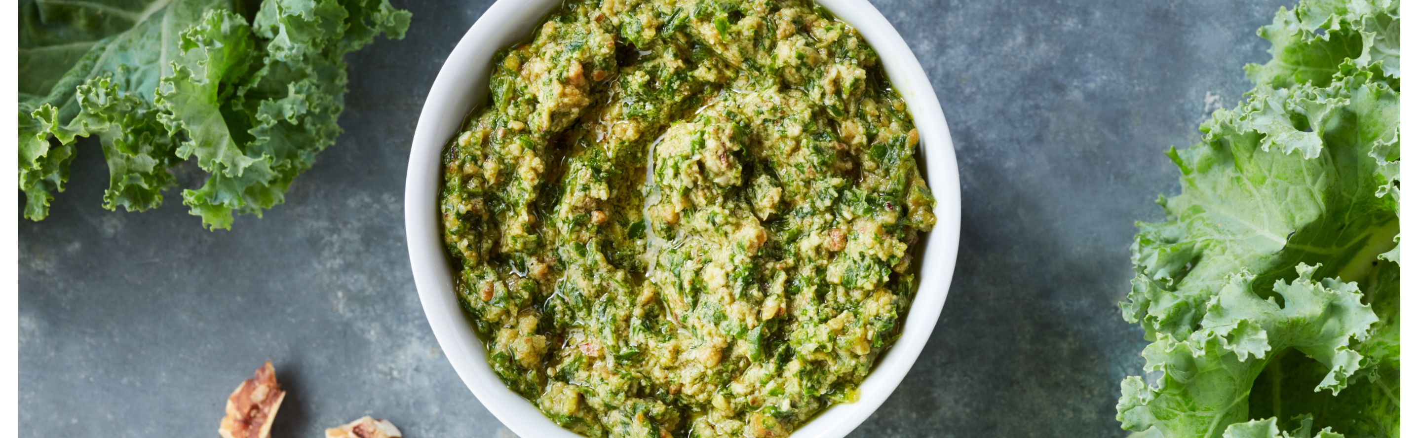 Fresh pesto in a white bowl next to kale