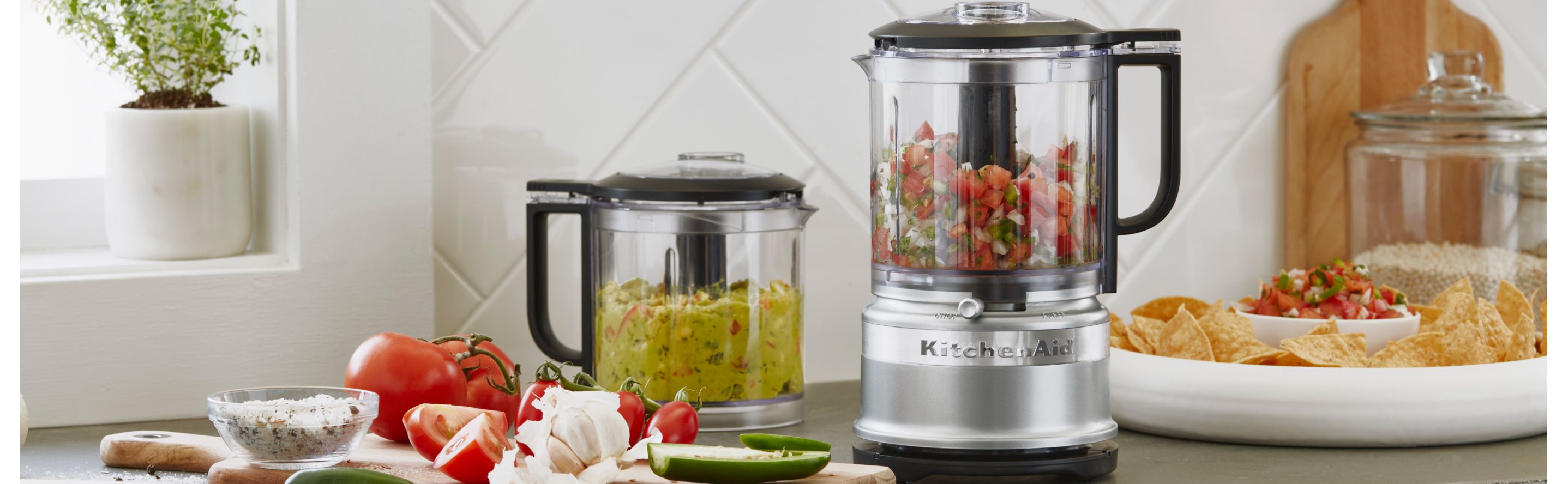 A KitchenAid® food processor and food chopper with freshly made salsa and guacamole on a modern kitchen counter.