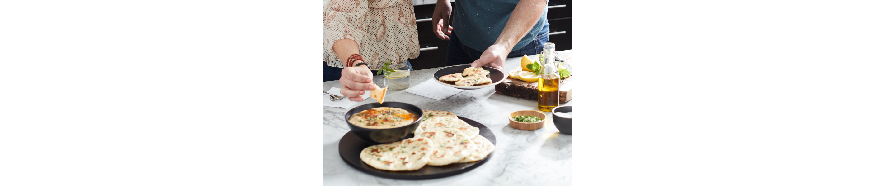 Person dipping pita bread into dish of baba ganoush next to whole pita pieces