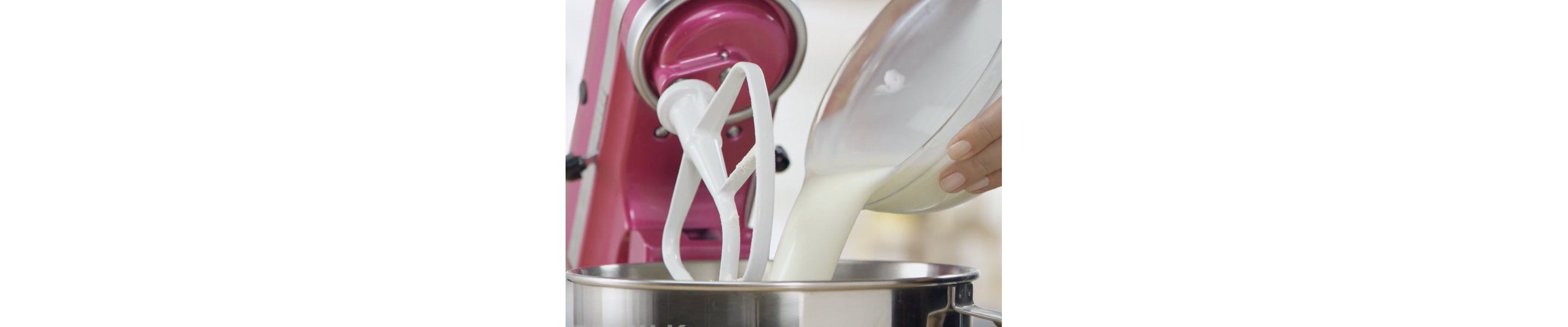 Person pouring milk from mixing bowl into stand mixer bowl