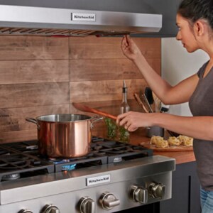 A person monitoring a saucepan boiling on a KitchenAid® cooktop