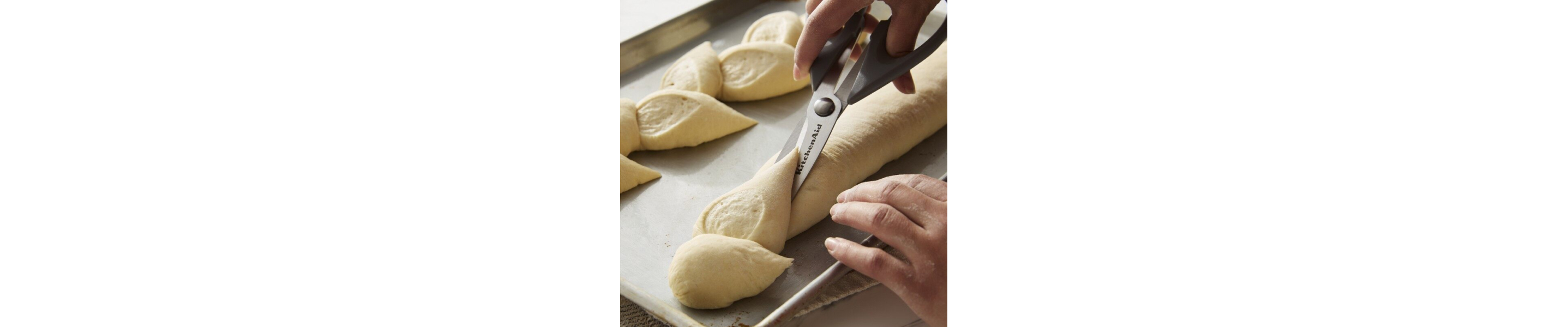Person using kitchen scissors to score bread dough on a baking sheet