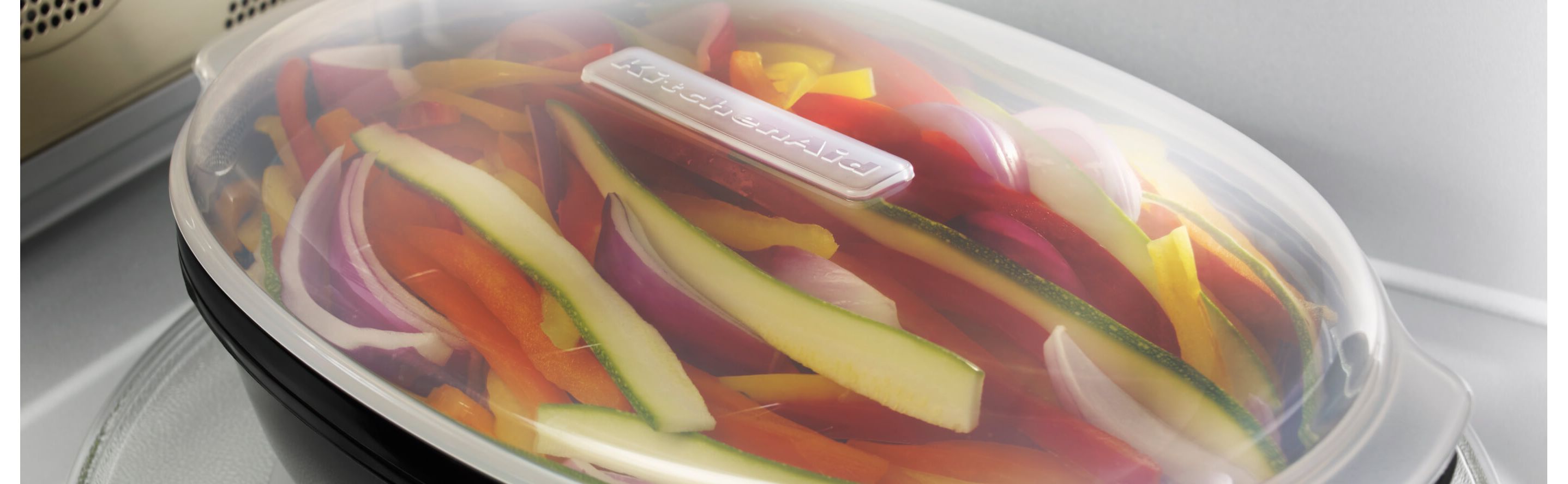 Sliced vegetables in a KitchenAid® steaming container in a microwave