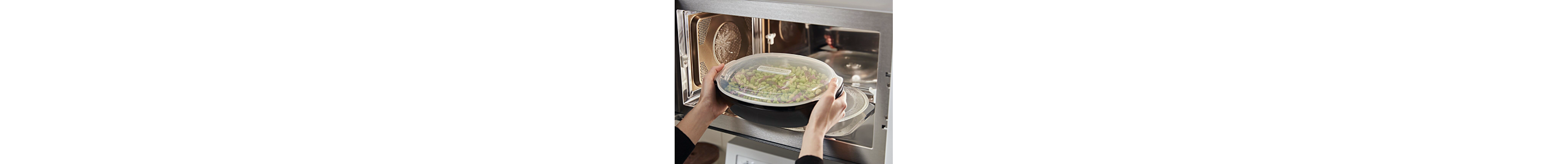 Person removing bowl of vegetables from microwave