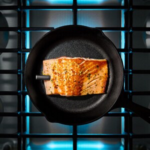 An overhead image of salmon cooking on a gas stovetop in a pan