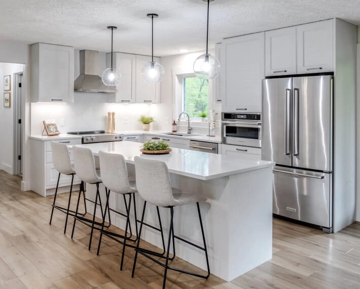 A bright white kitchen island with stool seating and pendant lights overhead