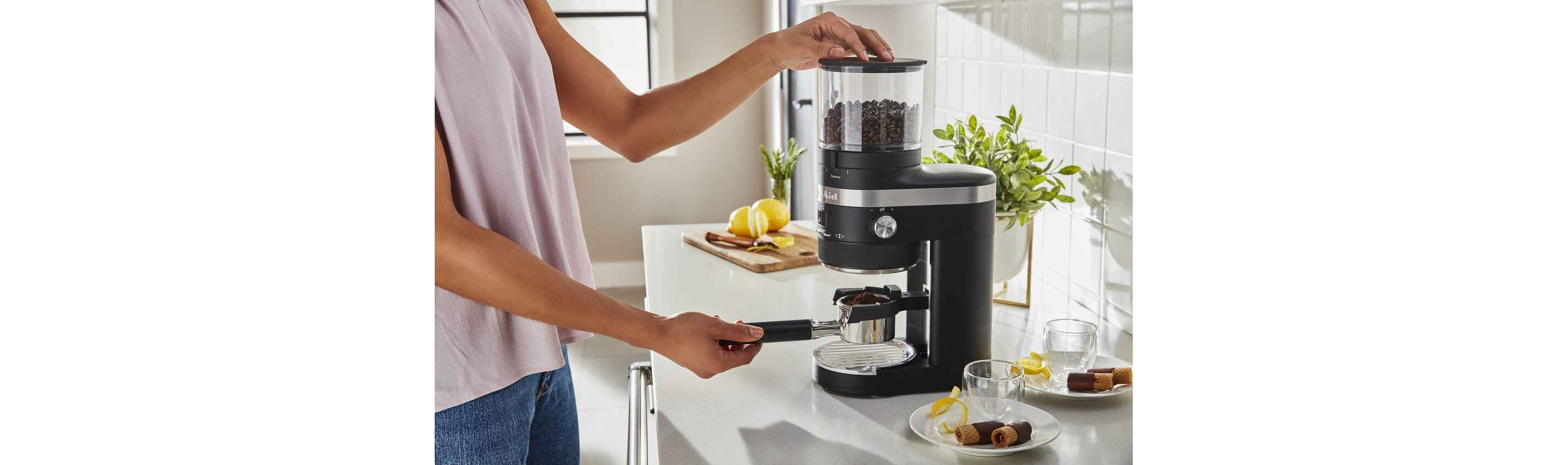 Woman using a black Kitchenaid® coffee grinder in bright kitchen