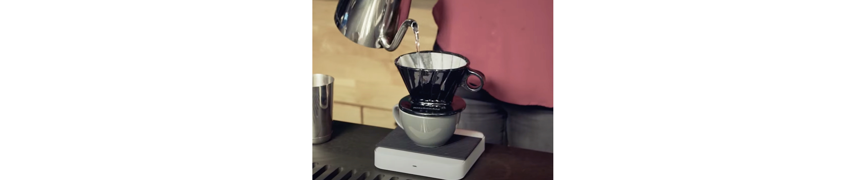 Maker pouring boiled water from electric kettle into pour over coffee filter