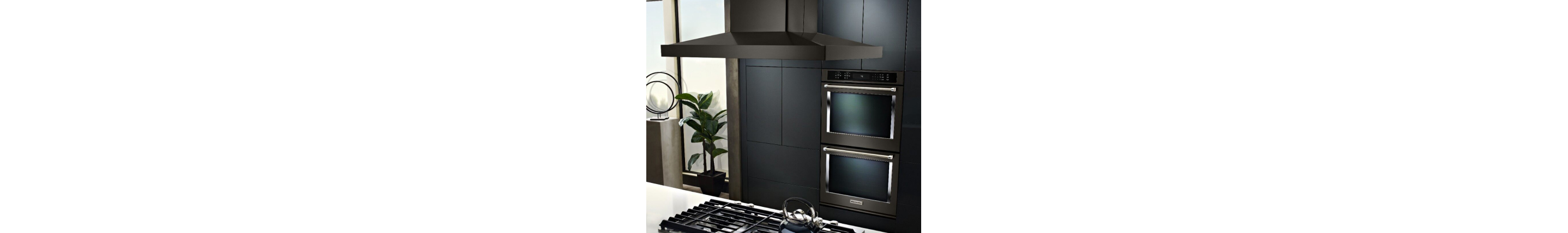 Island mount hood over a cooktop in an island countertop in front of a double wall oven