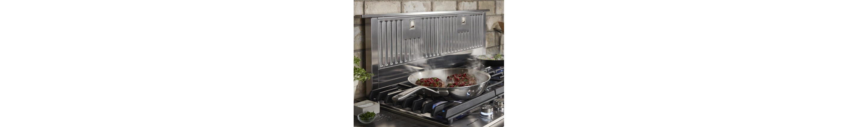 Filets cooking in a pan on a cooktop with a downdraft range hood behind it