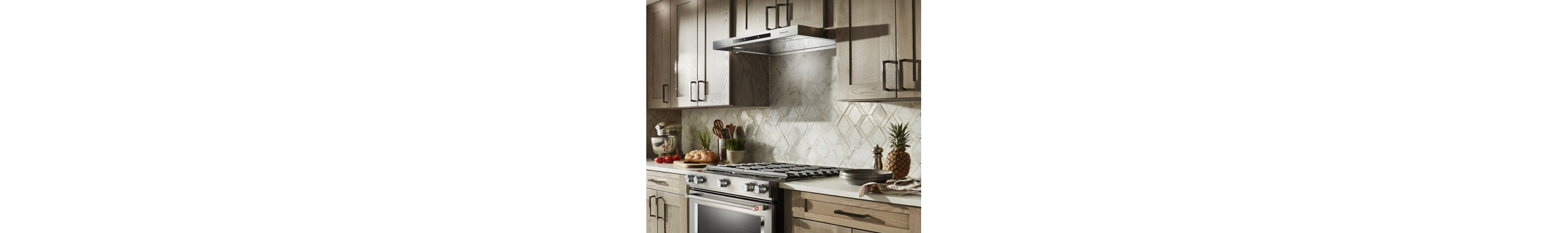 Low profile under cabinet hood between light wood cabinets over a slide-in range