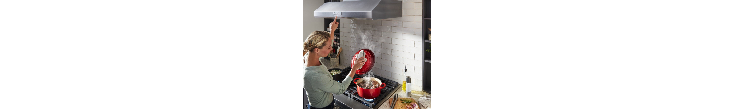 Woman cooking on a gas cooktop and turning on the wall mount hood