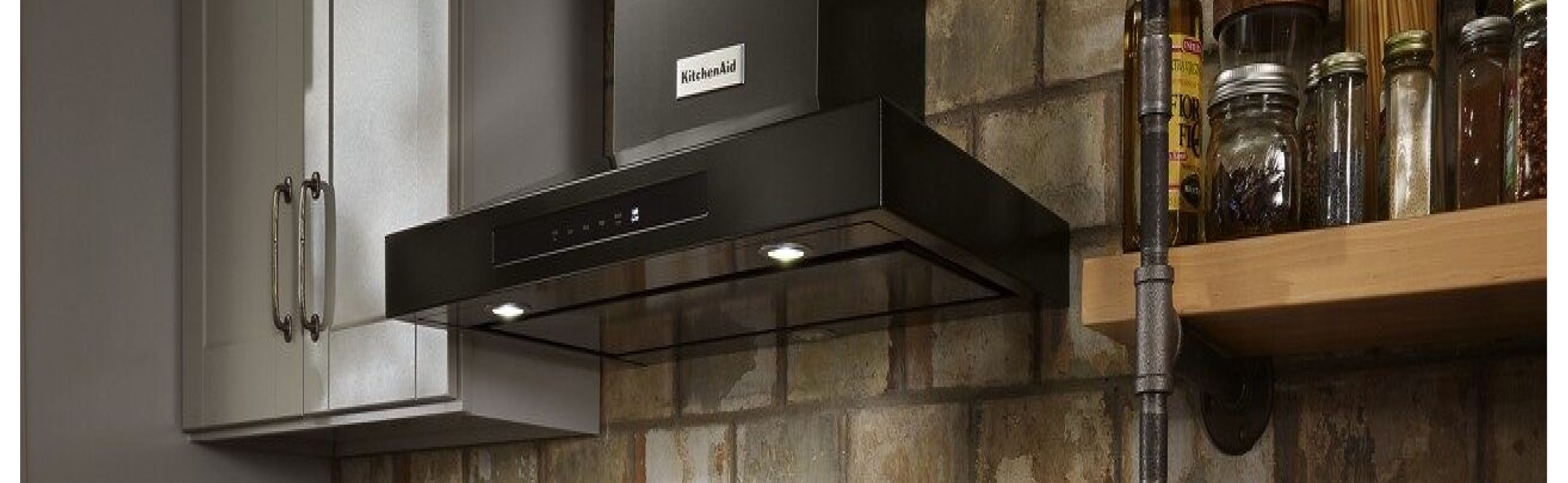 Black KitchenAid® wall mount hood in a kitchen in front of a brick wall