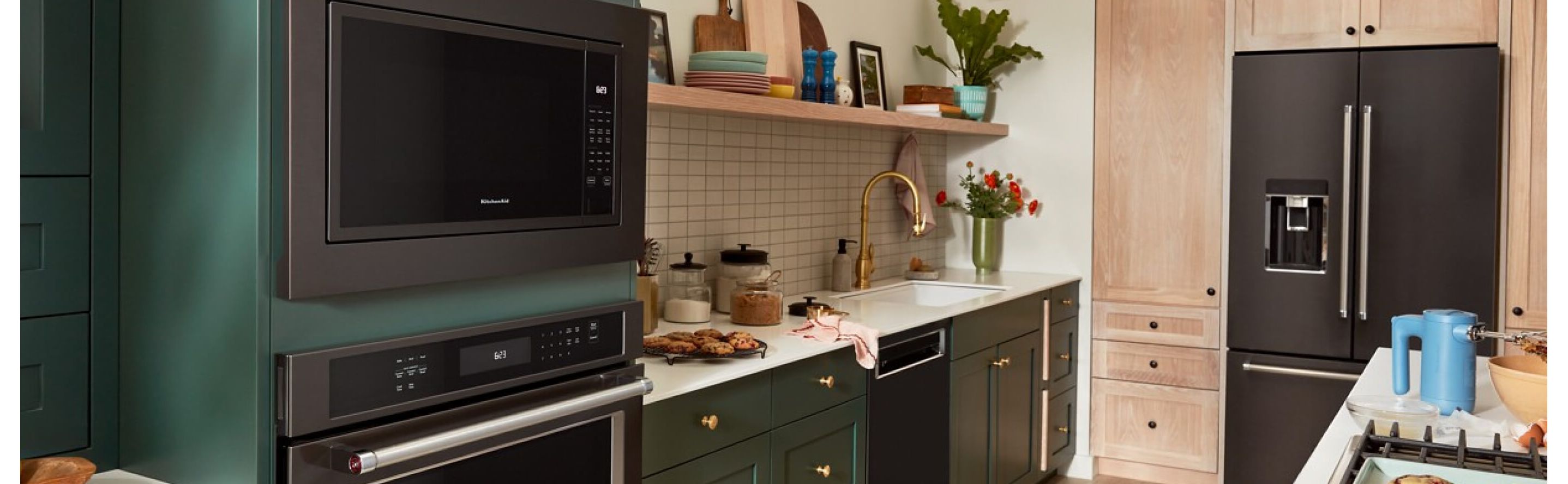 Suite of black stainless steel KitchenAid® appliances in green and natural brown cabinetry