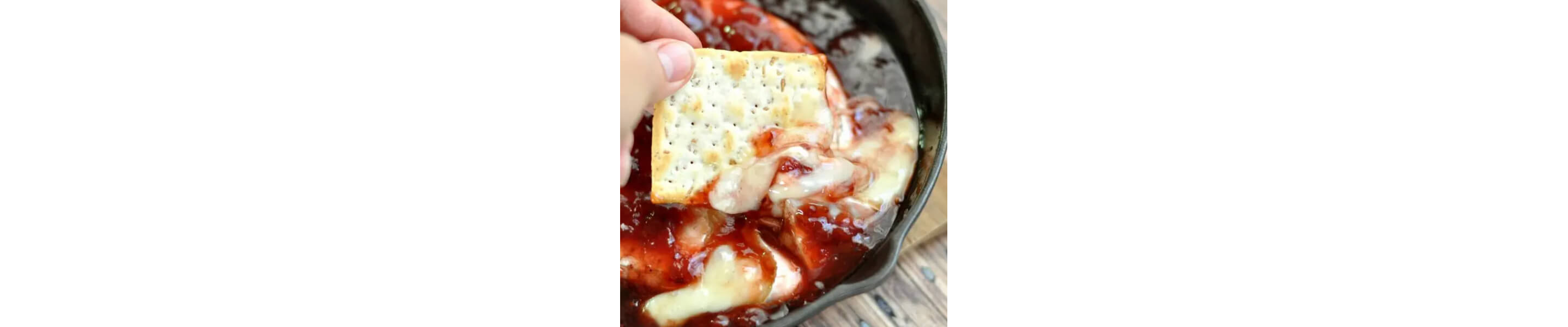 Cracker dipping into baked brie