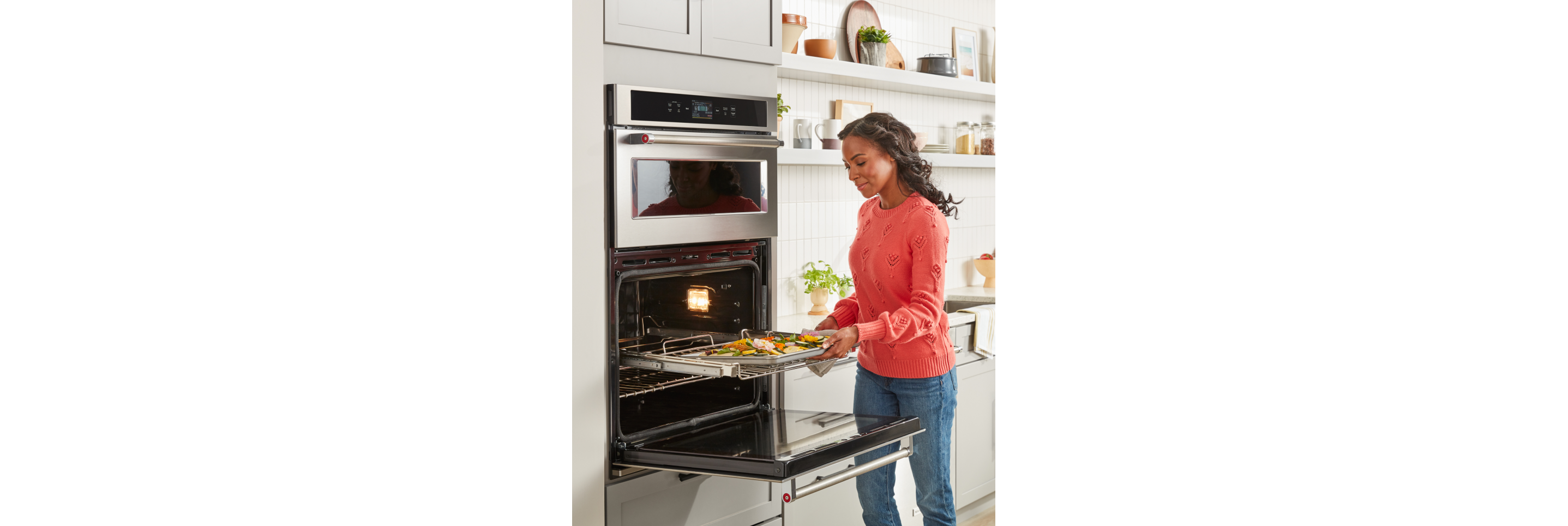 A woman pulling a baking sheet out of a KitchenAid® wall oven.
