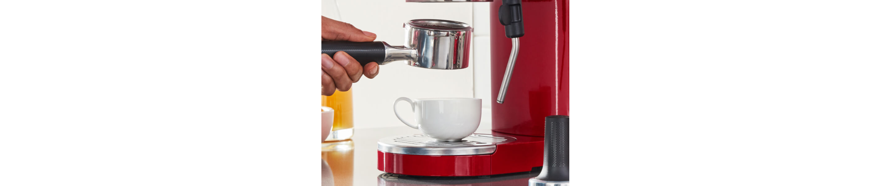Person holding espresso machine portafilter above teacup