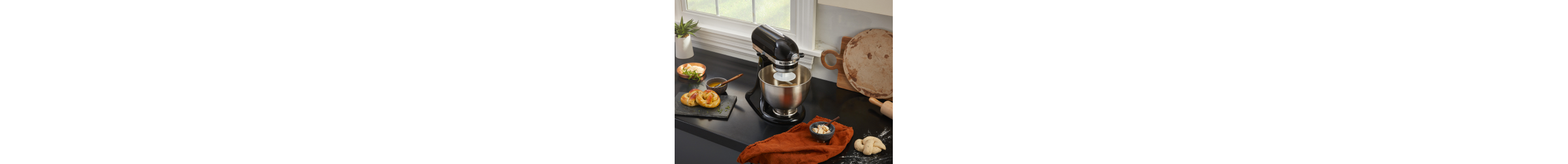 Black KitchenAid® stand mixer on black countertop next to homemade pretzels