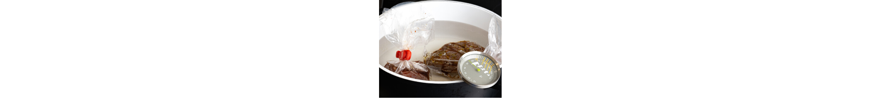 Two pieces of meat in sous vide bags placed inside a pot with a thermometer