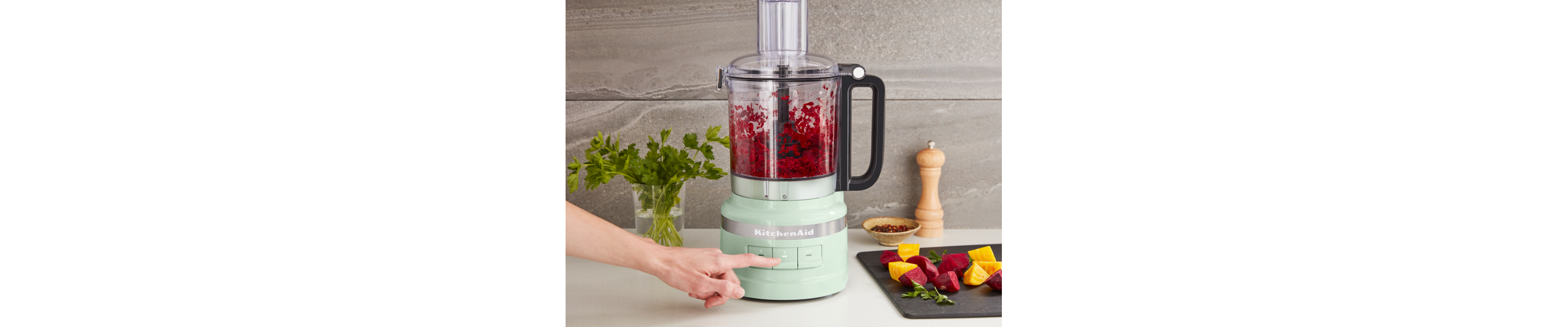 Person pulsing ingredients in a mint green KitchenAid® food processor
