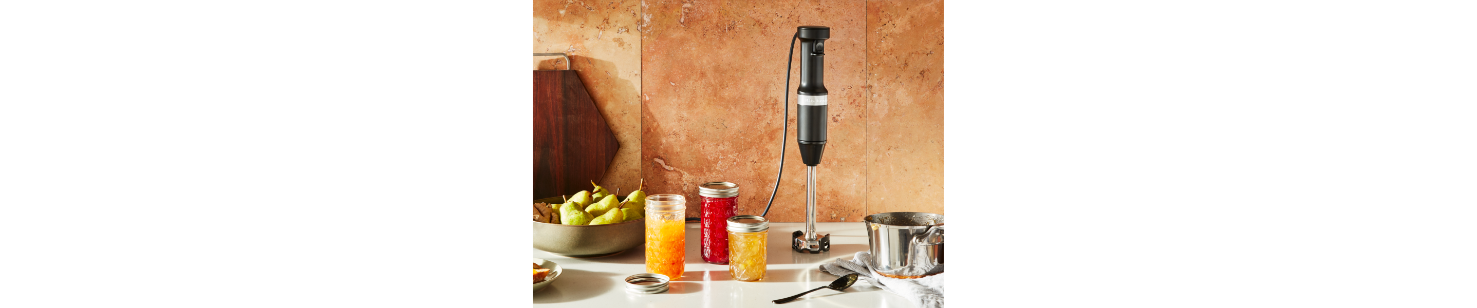 Black KitchenAid® hand blender next to jars of prepared jams