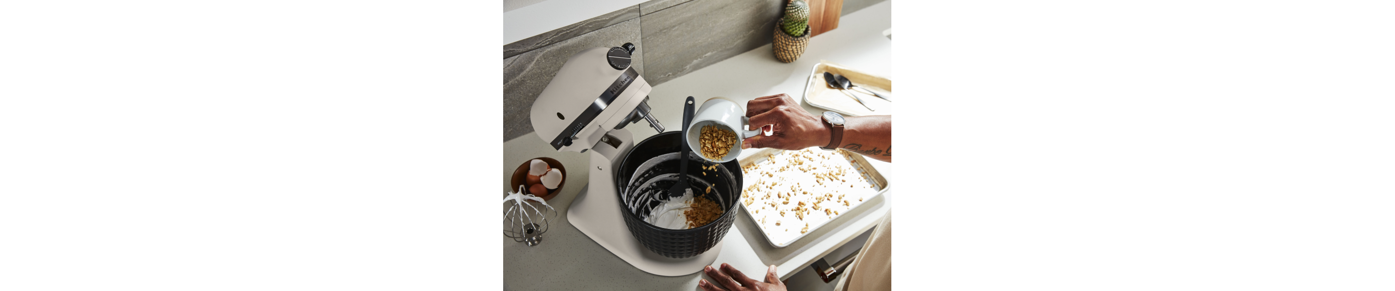 Person pouring ingredients into a white KitchenAid® stand mixer
