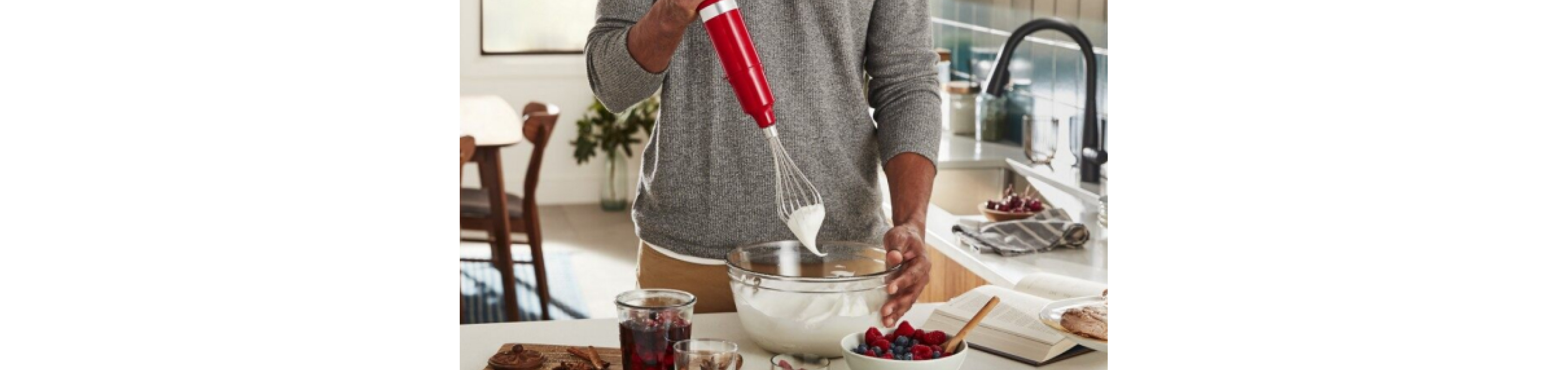 A person whipping cream with an immersion blender and whisk accessory.