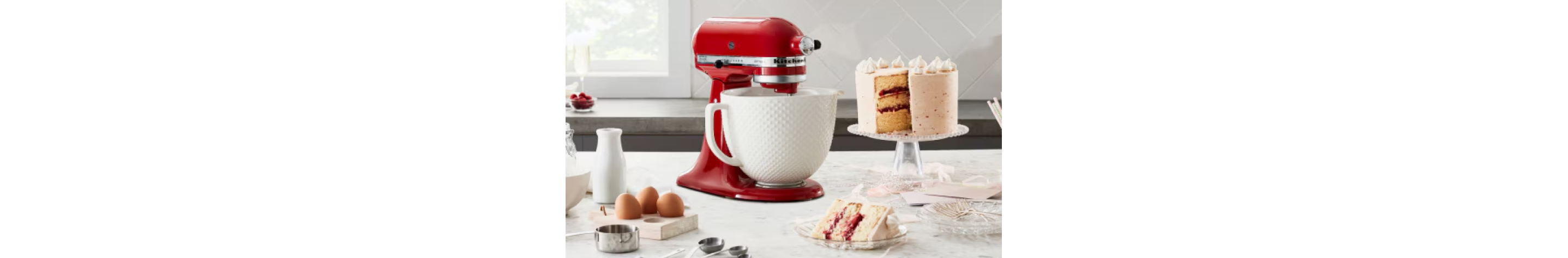 A red KitchenAid standmixer with a cake on a stand nearby