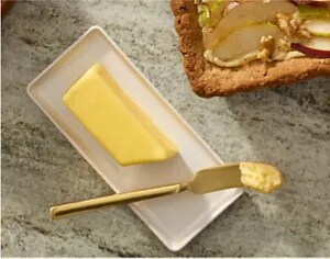 A stick of butter on a butter plate with a brass spreader
