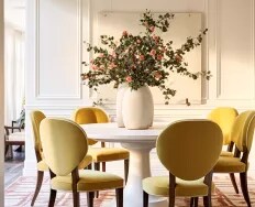 A flower arrangement on a dining room table with pale yellow upholstered dining chairs