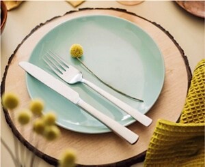 A tablesetting for one with a charcoal gray napkin, a glazed teal plate and decorative yellow flowers
