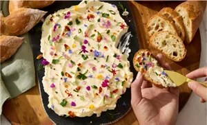 A person spreading flower-studded butter on a slice of baguette