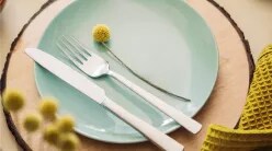A tablesetting for one with a charcoal gray napkin, a glazed teal plate and decorative yellow flowers