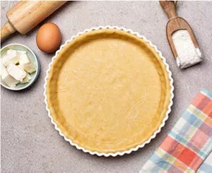 A tart crust and various baking implements and ingredients on a grey countertop.