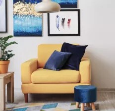 A rich yellow armchair with navy blue velvet pillows and a footstool