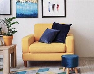 A rich yellow armchair with navy blue velvet pillows and a footstool