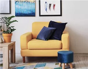 A rich yellow armchair with navy blue velvet pillows and a footstool