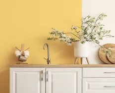 A kitchen sink set in a wooden countertop, with white cabinets and a bold yellow wall.