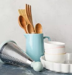 A grater and pitcher in robin's egg blue alongside wooden utensils and white dishes