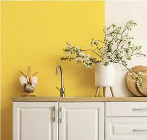 A kitchen sink set in a wooden countertop, with white cabinets and a bold yellow wall.