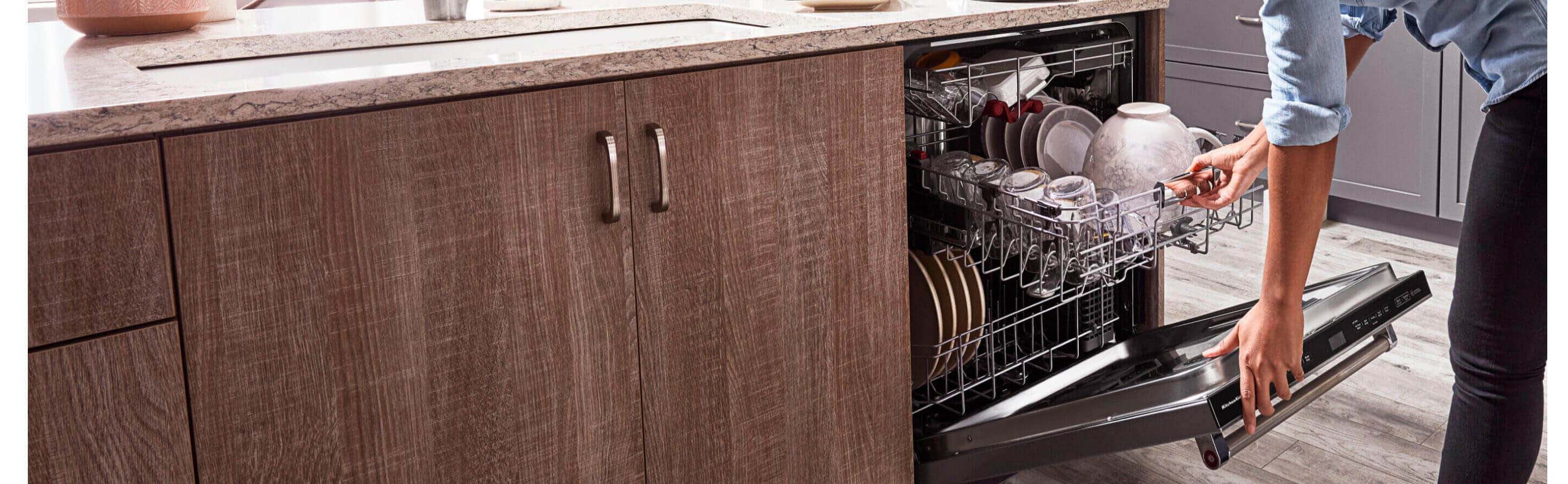 Hands opening a top control built-in dishwasher next to wood grain cabinets