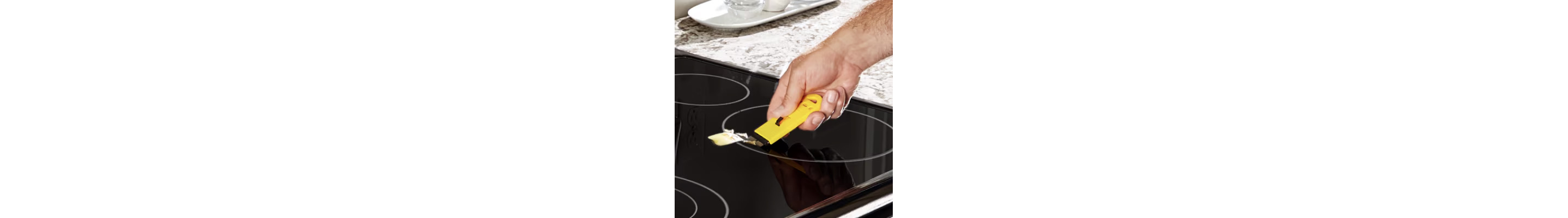 Hand using a scraper to clean an induction cooktop