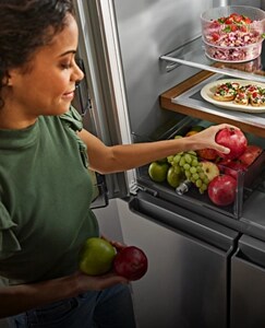 A person placing produce into a refrigerator drawer.